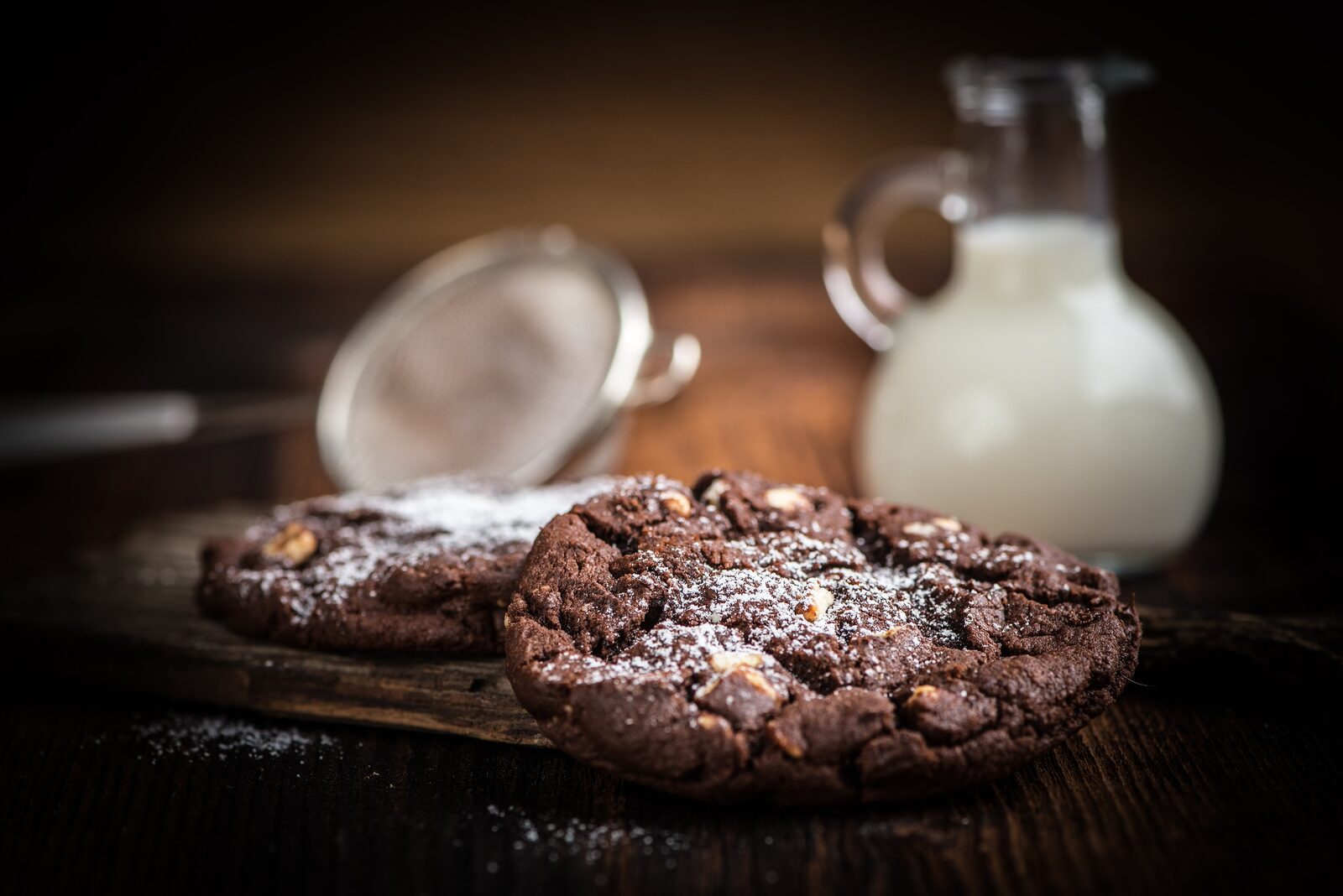 Dark chocolate cookies beside a jug of milk in low light